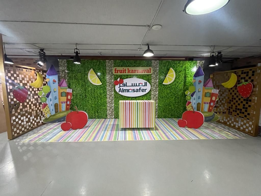 جدارية فعالية Fruit Karnaval لشركة Almosafer بخلفية عشب صناعي وشخصيات كرتونية