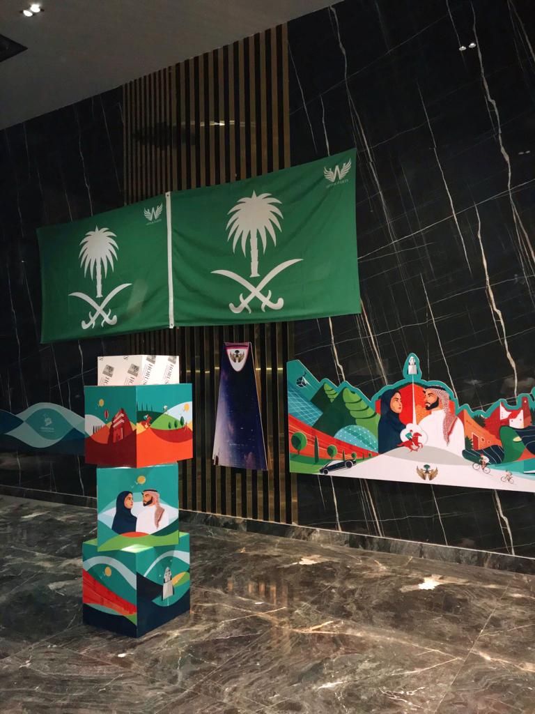 أعلام المملكة العربية السعودية وعمود مزخرف وجدارية فنية